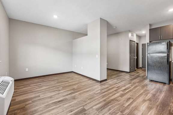 Spacious studio apartment with wood-style flooring, recessed lighting, an open layout, and a compact kitchen with black appliances.
