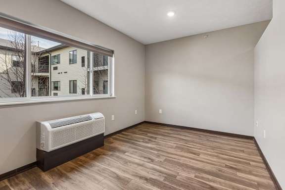 Bright studio apartment living area with wood-style flooring, a large window, and abundant natural light.