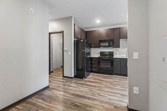 Open studio apartment with wood-style flooring, a modern kitchen with dark cabinetry, and a spacious, flexible layout.