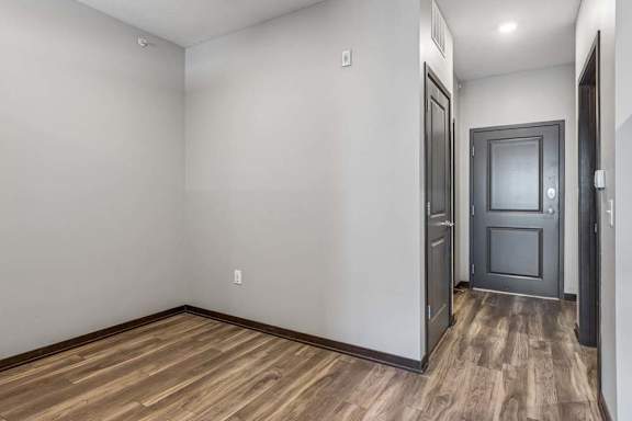 Studio apartment alcove with wood-style flooring, neutral finishes, and an open hallway leading to the entry and kitchen.