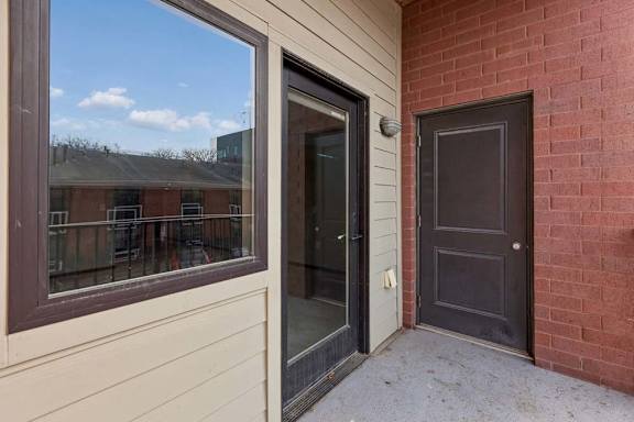 Covered apartment entry patio with a private front door, large window, and brick exterior.