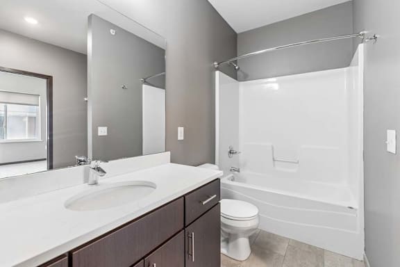 Bright apartment bathroom with a single-sink vanity, large mirror, and a tub and shower combination with neutral finishes.
