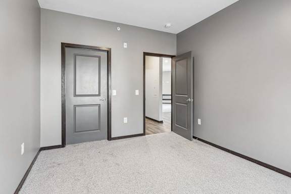 Carpeted apartment bedroom with gray walls, double-door closet access, and an open doorway leading to the hallway.