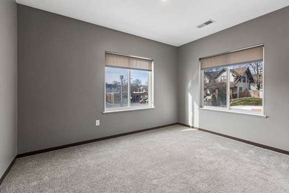 Spacious apartment bedroom with soft carpeting, two large windows, and abundant natural light.