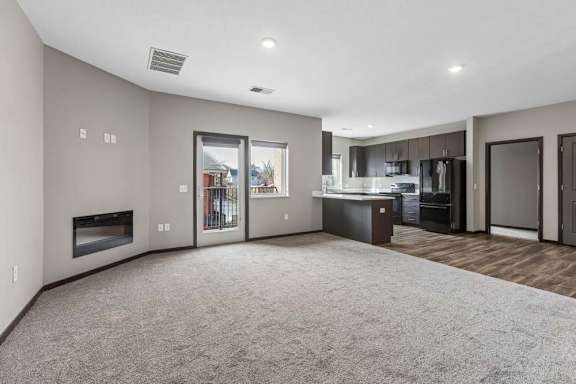 Bright apartment living room with plush carpeting, a modern kitchen, recessed lighting, a fireplace, and a sliding glass door to a private patio.