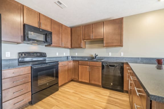 Large U-shaped kitchen with warm brown cabinets, black appliances, grey granite
