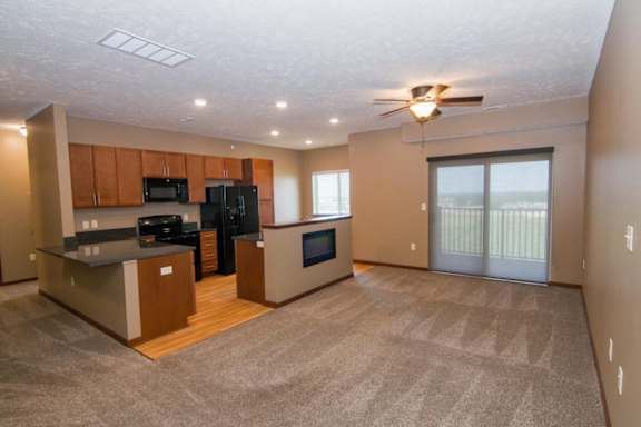 A spacious kitchen with black appliances connected to a carpeted living room
