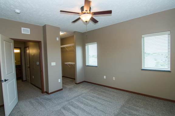 A room with a ceiling fan, open walk in closet, and carpeted floor.