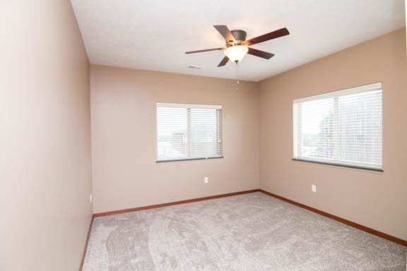 A room with a ceiling fan and two windows.