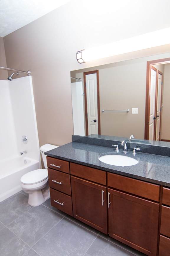 A bathroom with a toilet, vanity with storage, and mirror.