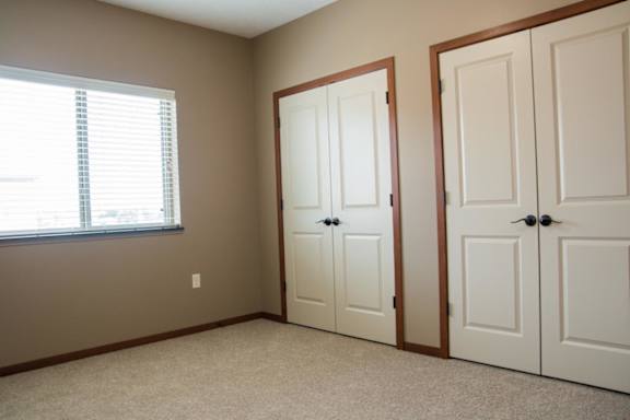 A room with a window, carpet, and 2 sets of double closet doors