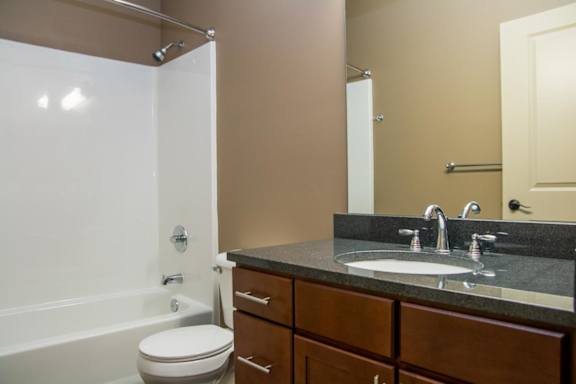 A bathroom with a white toilet, a black countertop, and a white bathtub.