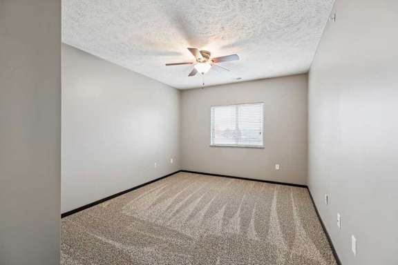 A carpeted bedroom with a large window and a ceiling fan.