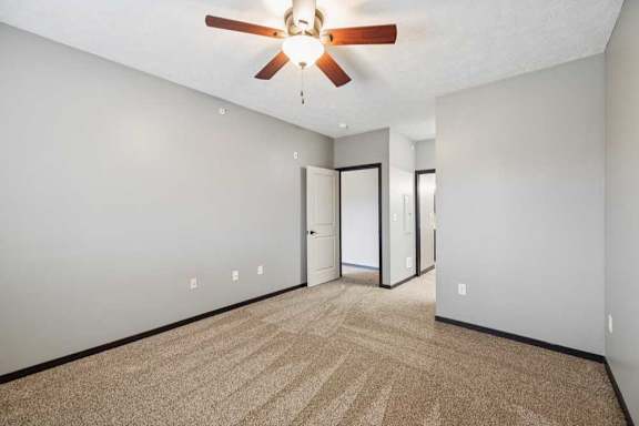 A carpeted bedroom with a ceiling fan, walk-in closet, and ensuite bathroom.