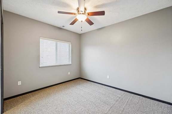 A carpeted bedroom with a window and a ceiling fan.