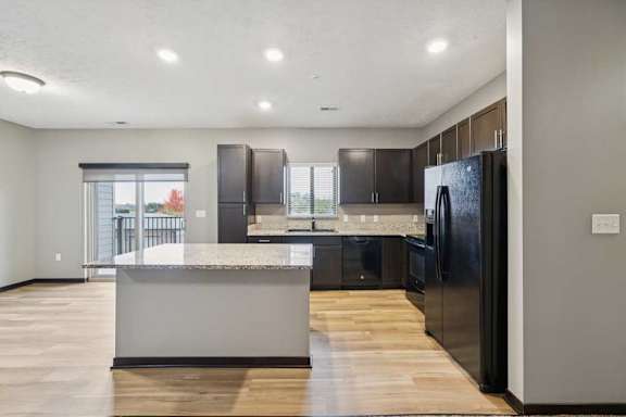A kitchen with dark cabinets, granite countertops, black appliances, a window over the sink, and a large island.