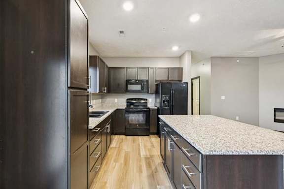 A kitchen with dark cabinets, granite counters, and black appliances.