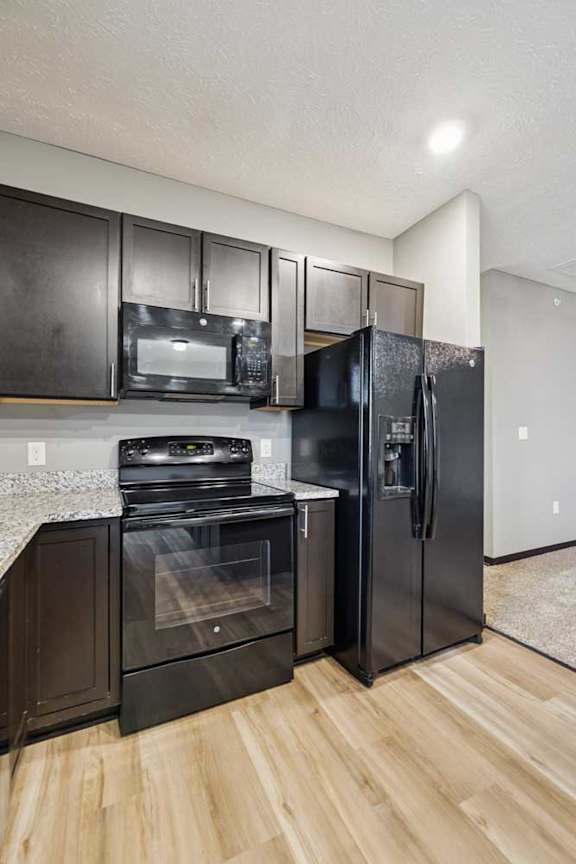 A close up of a black range and microwave in a modern kitchen with dark cabinets and light granite countertops.