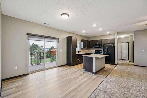 A dining area with a sliding glass door to a balcony, next to a modern kitchen with dark cabinets and granite countertops.