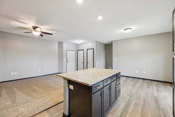 A kitchen island with dark cabinets in front of an open, carpeted living room.