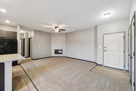A spacious, carpeted living room with an electric fireplace and a ceiling fan.
