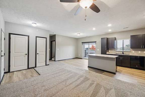 A spacious living room with carpeted flooring, open to a kitchen with a large island.