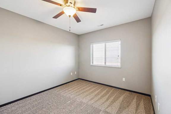 Empty bedroom with carpet, neutral walls, and a window with blinds providing natural light.
