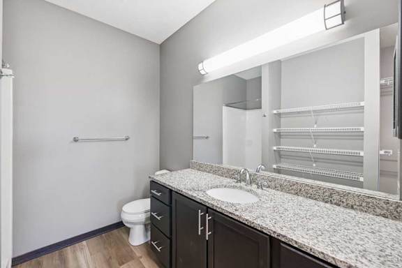Bathroom with long granite-look vanity, dark cabinets, large mirror, and open shelving visible through the reflection.