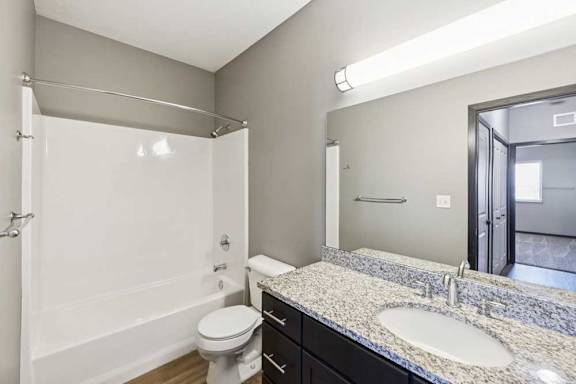 Bathroom with tub and shower combo, granite-look vanity, dark cabinetry, and large mirror.