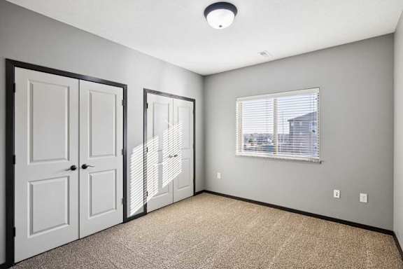 A room with a carpeted floor, two doors, and a window with blinds.