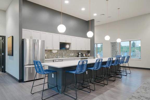 Modern resident lounge kitchen with expansive island seating, white cabinets, mosaic tile backsplash, and contemporary finishes.