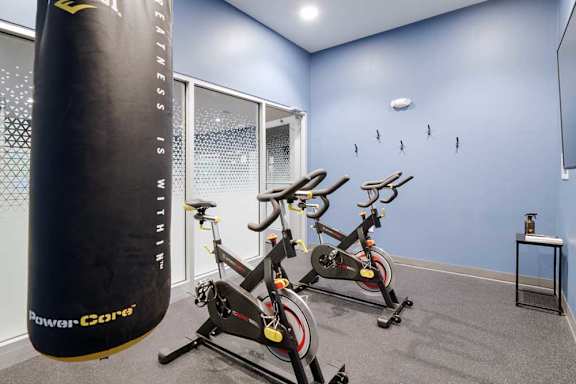 Fitness room featuring stationary bikes, a punching bag, blue accent walls, and mounted TV for resident workouts.