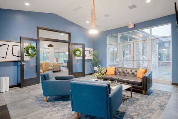 Community lounge with upholstered seating, fireplace, and floor-to-ceiling windows creating a bright, welcoming atmosphere.