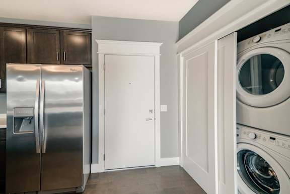 A kitchen with a refrigerator, a door to hallway and closet with stacked washer and dryer.