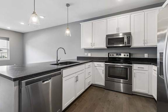 White cabinetry and dark countertops frame this apartment kitchen, complete with stainless steel appliances, pendant lights, and a peninsula sink.