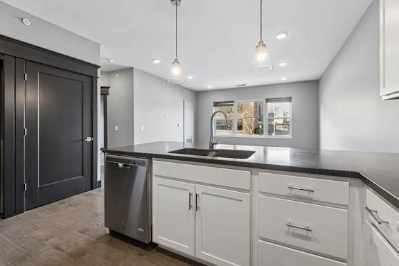 Long kitchen peninsula with an undermount sink, white cabinetry, dark countertop, pendant lighting, and an open view into the living area.