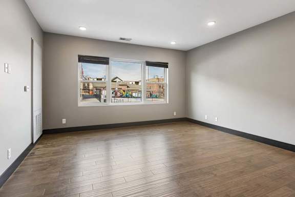 Wide windows fill this open apartment living room with natural light, complemented by gray walls, dark trim, and wood-look flooring.