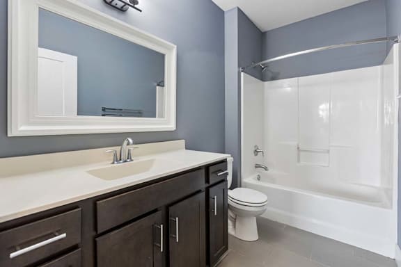 Deep espresso cabinetry and a white vanity top add contrast to this apartment bathroom with gray walls and a tub-shower combo.