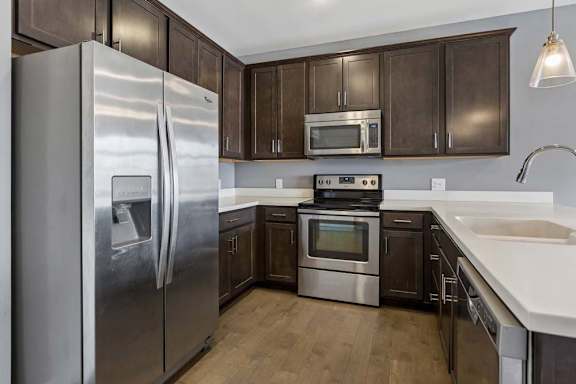 Dark wood cabinetry wraps around this apartment kitchen, paired with white counters, stainless steel appliances, and a peninsula sink.
