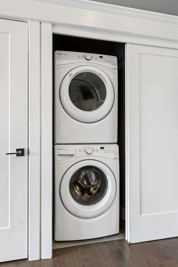 Stacked washer and dryer fit neatly into a recessed apartment laundry closet with white sliding doors and trim.