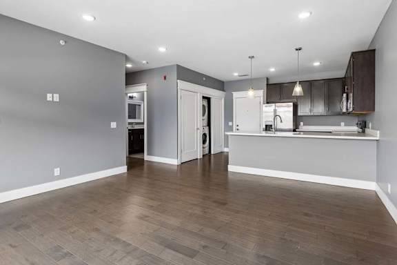 Open apartment living area leads into a kitchen with dark cabinetry, a breakfast bar, pendant lighting, and nearby in-home laundry.