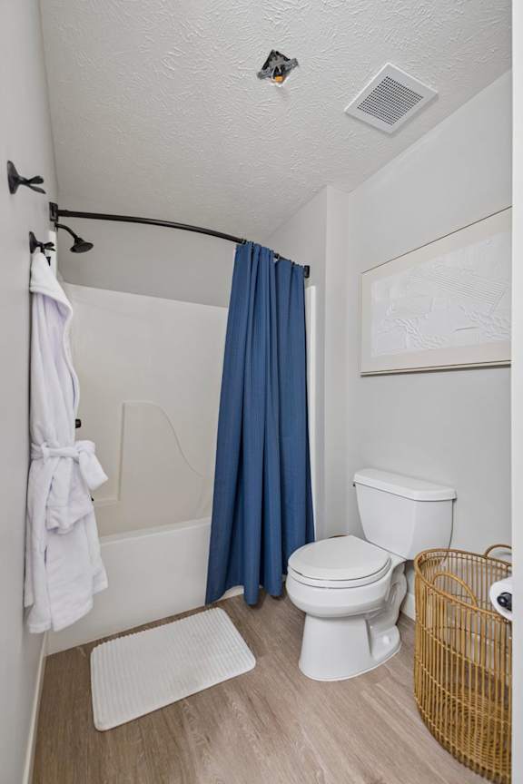 Apartment bathroom with blue shower curtain, wood-style flooring, and open shelving.
