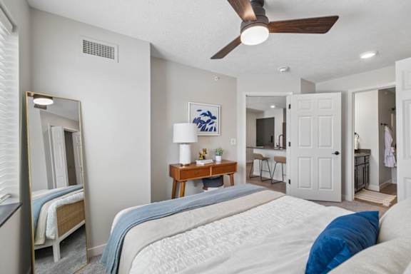 Apartment bedroom with ceiling fan, full-length mirror, and neutral finishes.