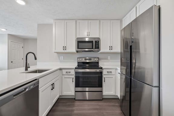 Apartment kitchen with white cabinetry, stainless steel appliances, and dark wood-style flooring.