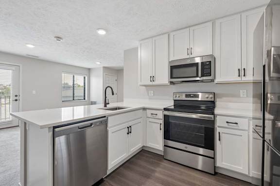 Apartment kitchen with white cabinetry, stainless steel appliances, and peninsula seating.