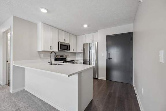 Apartment kitchen with white cabinetry, peninsula seating, and stainless steel appliances.