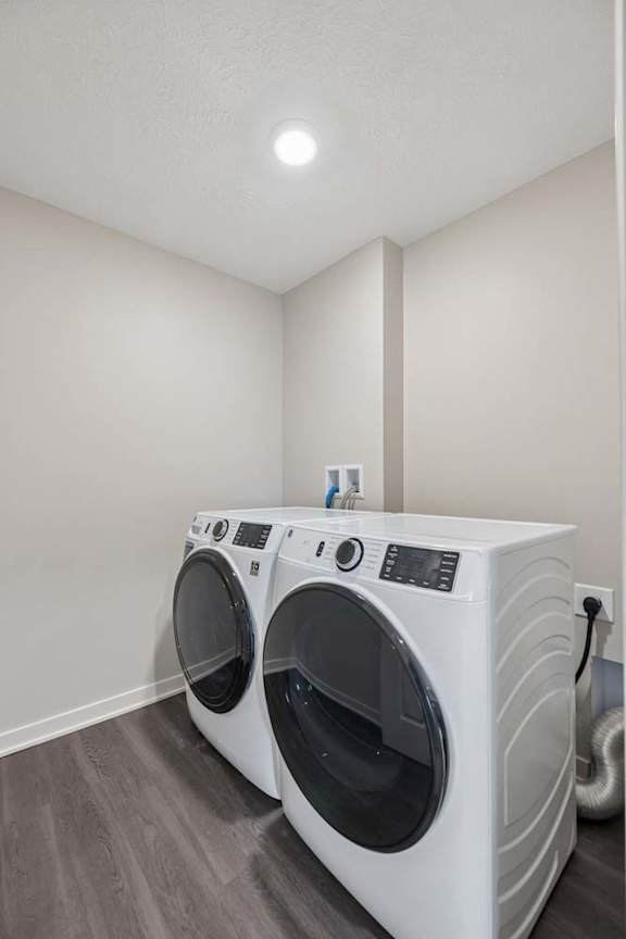 Apartment laundry room with side-by-side washer and dryer, wood-style flooring, and recessed lighting.