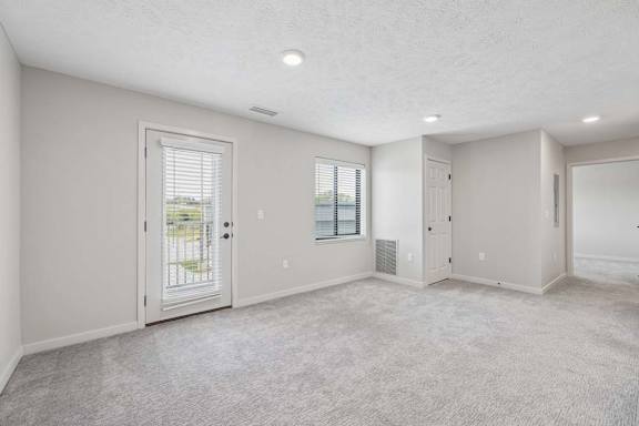 Open apartment living area with neutral carpeting, large window, and patio door with blinds.