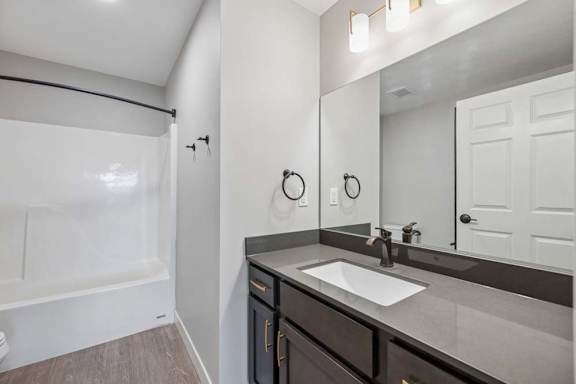 Apartment bathroom with a single-sink vanity, dark cabinetry, a large framed mirror, and a tub-shower combination with a white surround.