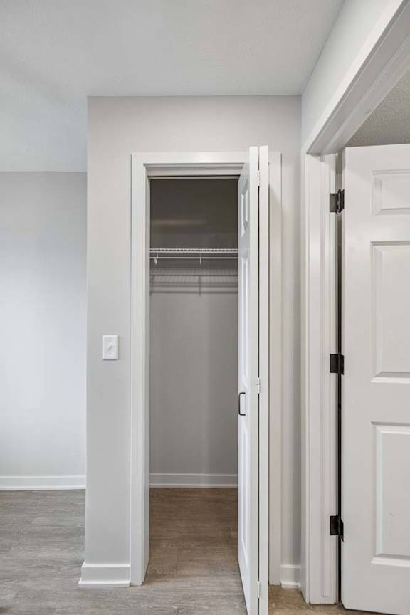 Walk-in apartment closet with built-in shelving, hanging rods, and neutral finishes, accessible through a white paneled door.